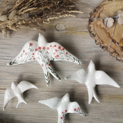 Figuras decorativas de pássaros de cerâmica branca com padrões florais, em mesa de madeira com ramos secos