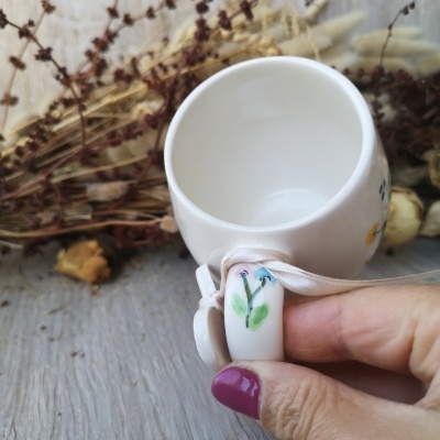 Copo cerâmico branco com pintura floral colorida na pega e flores secas ao fundo