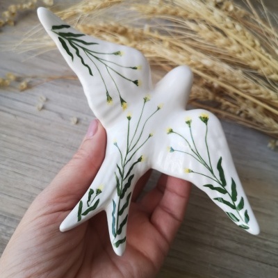 Escultura cerâmica de ave branca com flores amarelas e verdes nas asas