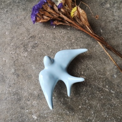 Figura em cerâmica azul clara de uma andorinha com flores secas ao lado sobre pedra cinzenta
