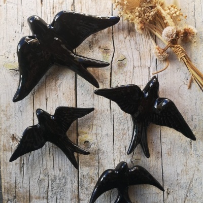 Figuras de pássaros pretos em cerâmica sobre madeira com ramo de flores secas