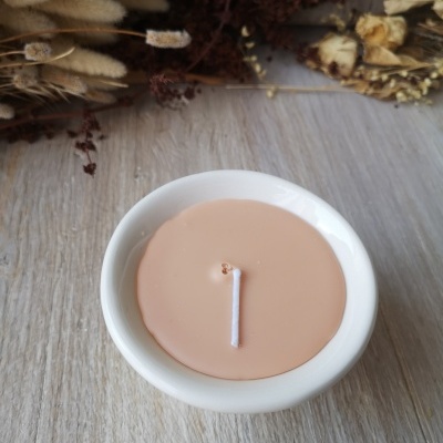 Vela castanha clara em recipiente branco com flores secas ao fundo