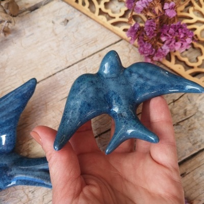 Estatueta pássaro cerâmica azul em mão com fundo madeira e flores secas