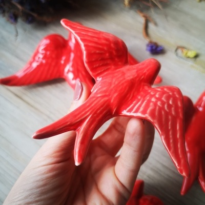 Figuras decorativas de pássaros vermelhos em cerâmica com textura, em mão e superfície de madeira com flores secas.
