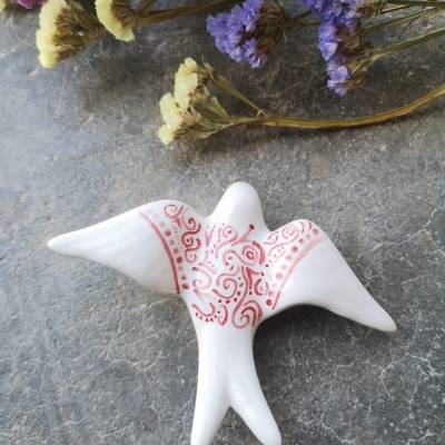 Figura decorativa em forma de pássaro branco com padrão vermelho e flores secas ao fundo