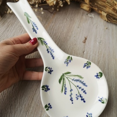 Colher de cerâmica branca com padrão floral azul e verde sobre madeira clara