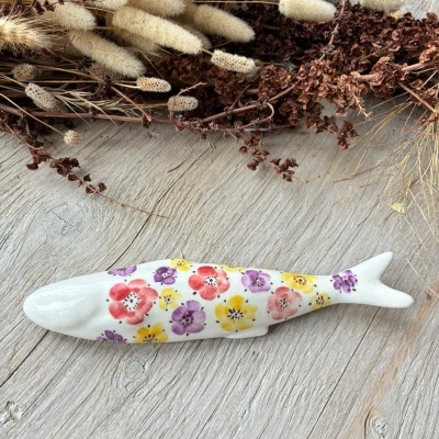 Peixe de cerâmica branca com flores coloridas sobre madeira clara com flores secas ao lado