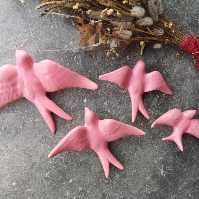 Figuras decorativas de pássaros cor-de-rosa sobre superfície de pedra cinzenta com flores secas ao fundo