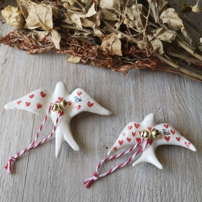 Figuras de pássaros em cerâmica branca com corações vermelhos e sinos dourados sobre superfície de madeira