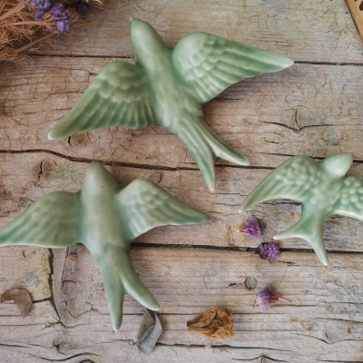 Três pássaros de cerâmica verde sobre madeira rústica com flores secas