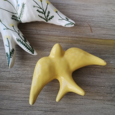 Figuras de pássaros em cerâmica, uma branca com padrão floral e outra amarela sobre madeira.