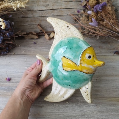 Peixe decorativo em cerâmica verde, amarelo e branco com mesa de madeira e ramos secos