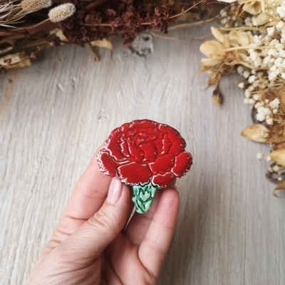 Broche em forma de cravo vermelho esmaltado brilhante segurado por mão