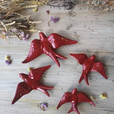 Esculturas de pássaros vermelhos em cerâmica sobre madeira com flores secas