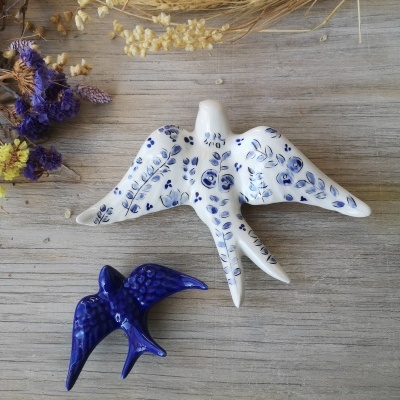 Duas aves decorativas em cerâmica em madeira clara com flores secas.