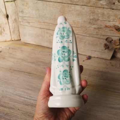 Figura decorativa em cerâmica branca com flores azuis, segurada em mão, sobre madeira rústica