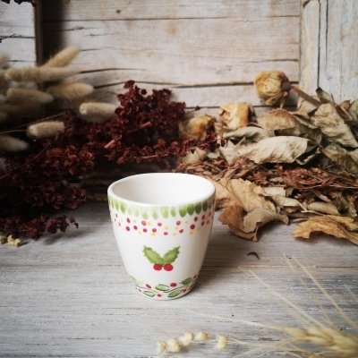 Copo de cerâmica com padrão verde e vermelho em superfície de madeira com plantas secas ao fundo