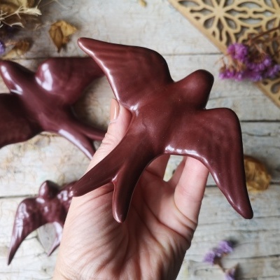 Esculturas cerâmicas de andorinhas castanhas sobre mesa de madeira