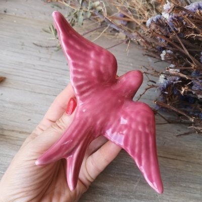 Pássaro decorativo de cerâmica cor-de-rosa brilhante na mão sobre fundo de madeira e galhos secos