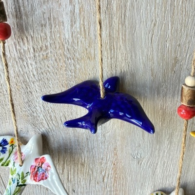 Pássaro azul em cerâmica vidrada pendurado em corda com outros pássaros em cerâmica decorada