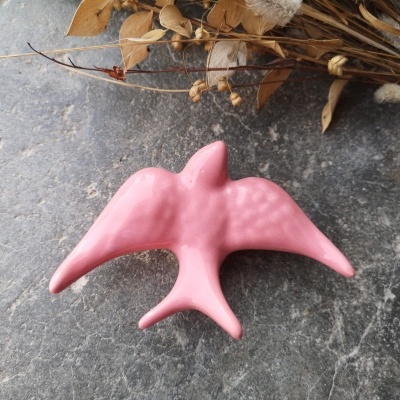 Figura decorativa rosa de pássaro sobre pedra com ramo seco ao fundo