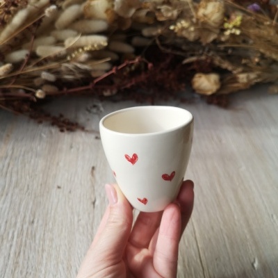 Copo de cerâmica branco com corações vermelhos e flores secas ao fundo