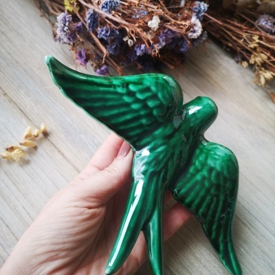 Escultura verde brilhante em forma de pássaro sobre madeira com ramos secos ao fundo