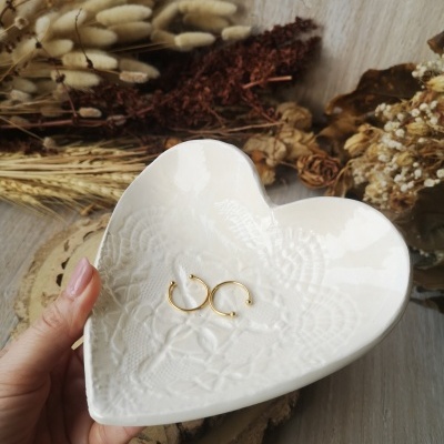 Prato de cerâmica branca em forma de coração com textura rendada e dois brincos dourados em argola
