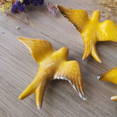 Figuras decorativas de pássaros amarelos com detalhes brancos sobre madeira clara com flores secas