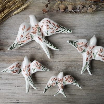Quatro pássaros decorativos em cerâmica branca com pintura floral sobre madeira clara.