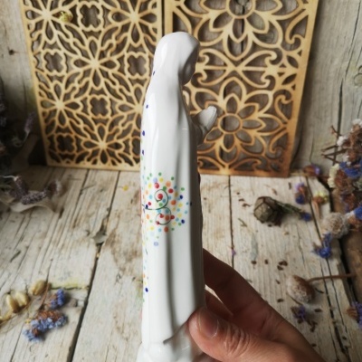 Estatueta branca em porcelana com padrão colorido, segurada por uma mão, sobre mesa de madeira rústica