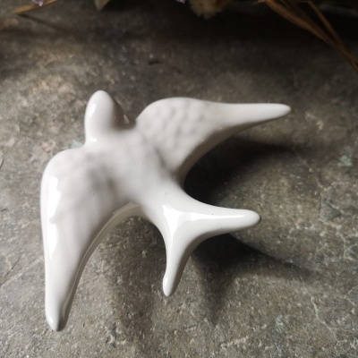 Figura em cerâmica branca de uma andorinha sobre pedra cinzenta