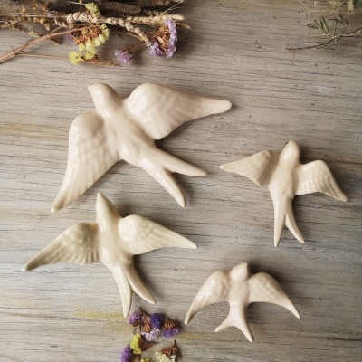 Quatro aves decorativas em cerâmica branca sobre madeira com flores secas