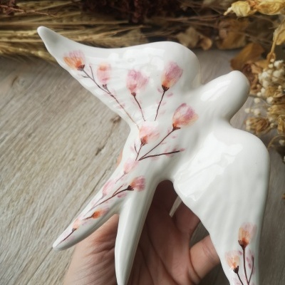 Escultura em cerâmica branca com pintura floral segurada à mão.