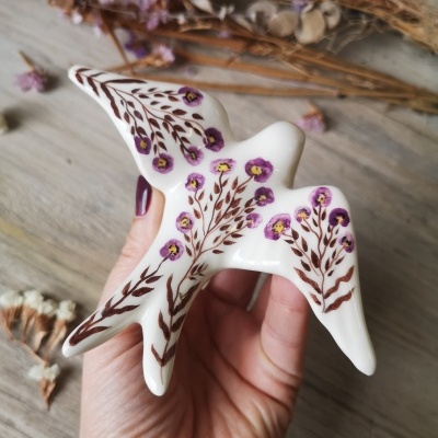 Figura de pássaro em cerâmica pintada com flores roxas e ramos castanhos