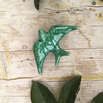 Pássaro decorativo verde em cerâmica sobre madeira clara com folhas