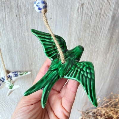 Pássaro decorativo verde em cerâmica com cordão e contas em fundo cinzento