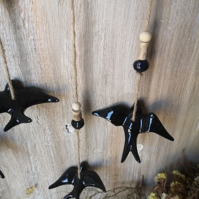 Móbile com pássaros cerâmicos pretos e contas de madeira pendurado numa parede de madeira