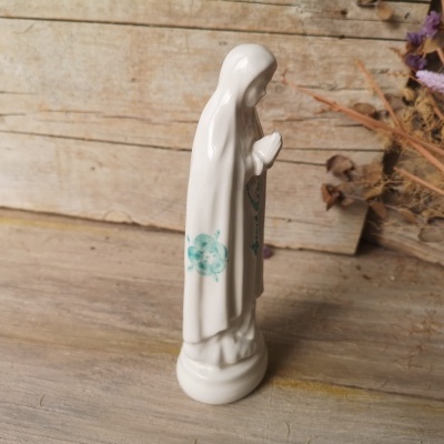 Estátua cerâmica branca de figura feminina com detalhes verdes em superfície e fundo de madeira com vegetação seca