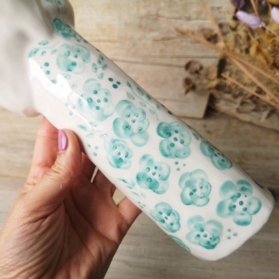 Frasco branco de cerâmica com flores azuis segurado à mão