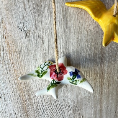 Pendentes de gaivota em cerâmica, uma branca com flores e outra amarela, penduradas com corda rústica.