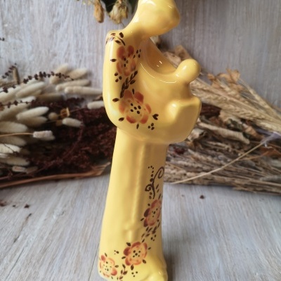 Estatueta de cerâmica amarela com flores decorativas e forma abstracta de figura segurando bebé