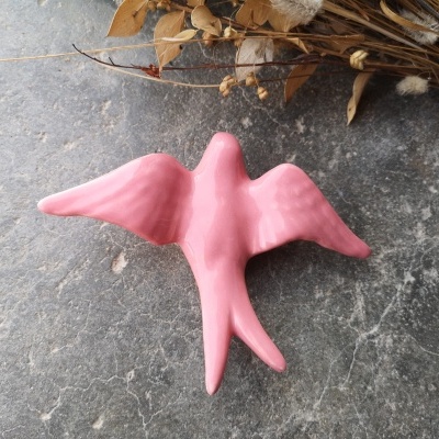 Escultura decorativa de pássaro rosa em superfície rústica com flores secas ao fundo