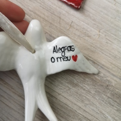 Figura decorativa de pássaro branco com texto 'Alegras o meu' e coração vermelho