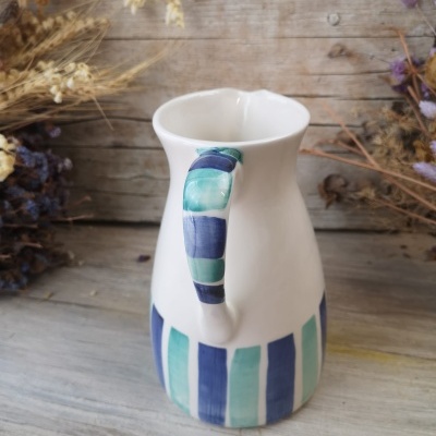 Jarro de cerâmica branca com riscas azuis e verdes e flores secas ao fundo