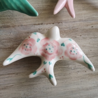 Estatueta cerâmica pássaro branca com flores rosas e verdes sobre madeira