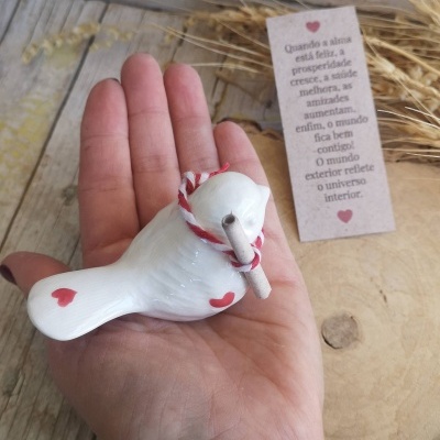Pássaro decorativo de cerâmica branca com corações vermelhos e cordão vermelho e branco na mão.