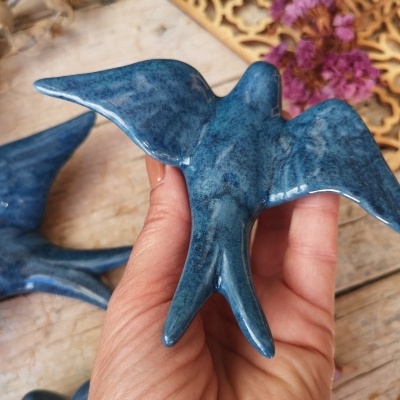 Figurinha de pássaro azul em cerâmica brilhante segurada por mão sobre mesa de madeira com flores secas