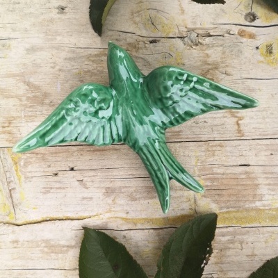 Pássaro decorativo verde em cerâmica sobre superfície de madeira