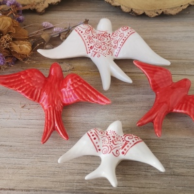 Estatuetas de pássaros em cerâmica vermelha e branca sobre mesa de madeira